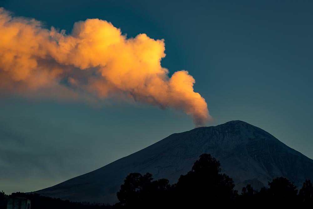 The glow of sunset lights up the billowing plume wafting from the rumbling volcano.